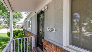 Une maison d’habitation avec une façade en briques, un porche blanc doté d’une balustrade et une porte noire.