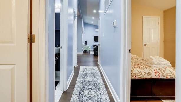 Un couloir étroit, orné d’un tapis à motifs, mène à une chambre à coucher où se trouvent un lit et une table de chevet.