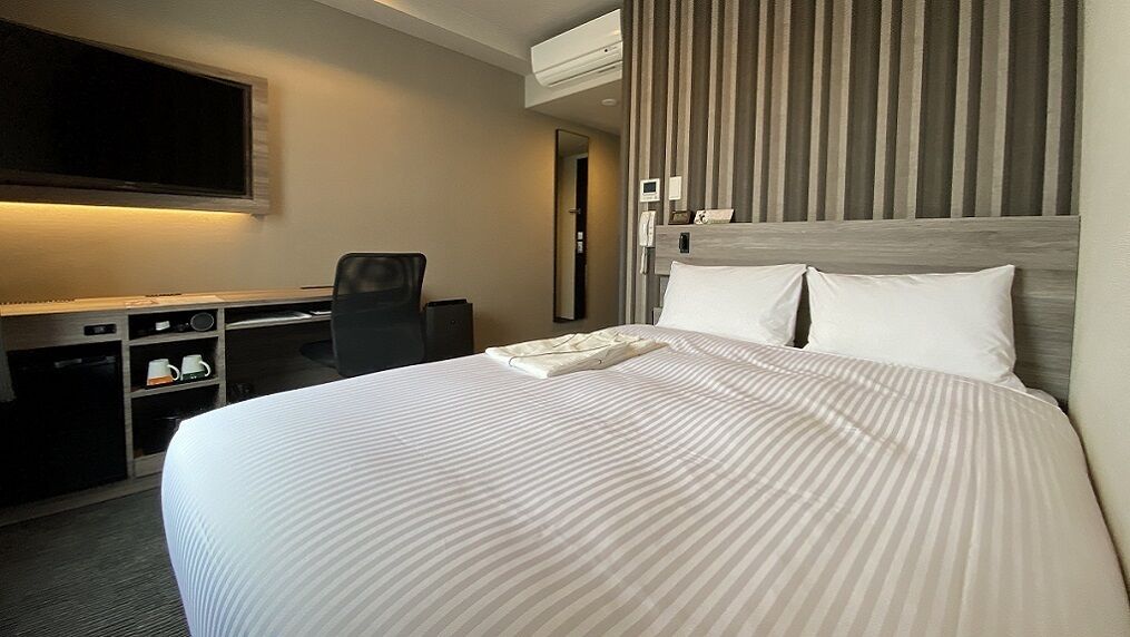 A hotel room with a bed, a desk, a chair, a TV, and a mirror.