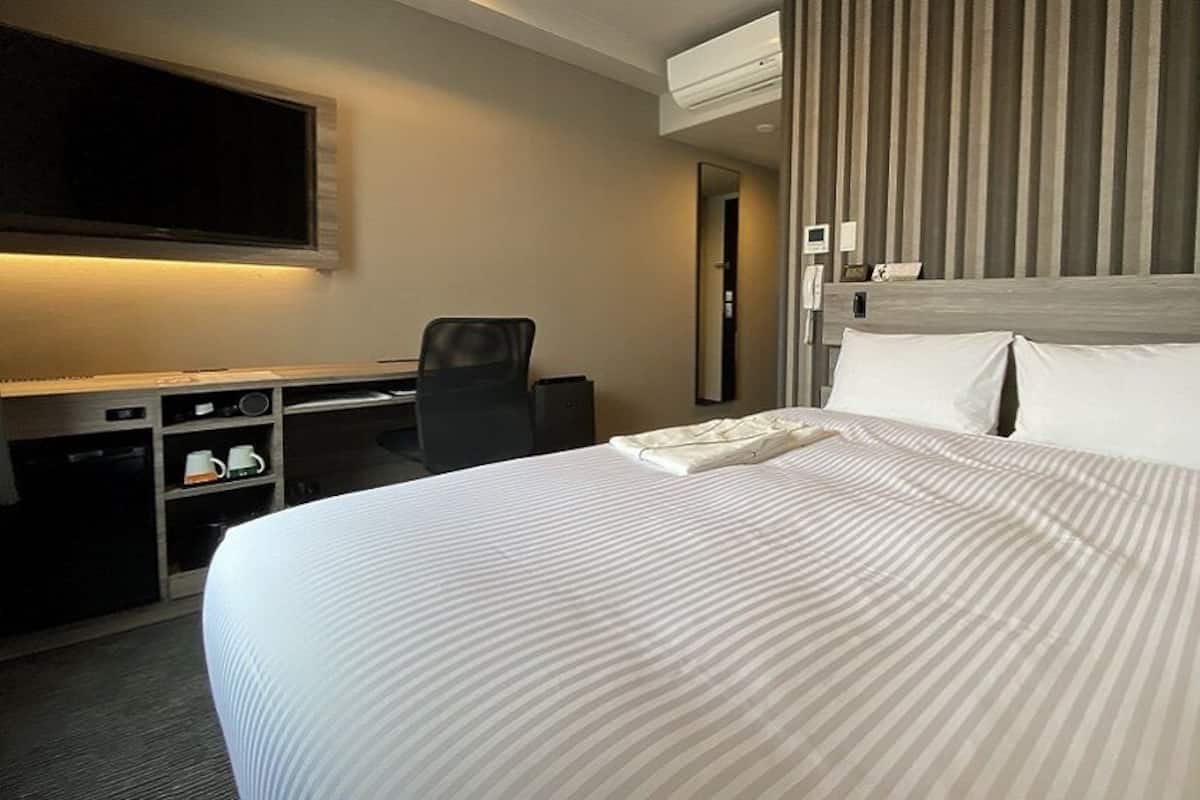 A hotel room with a bed, a desk, a chair, a TV, and a mirror.