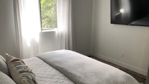 Um quarto com uma cama, uma janela com cortinas e uma televisão presa na parede.