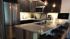 Cozinha moderna com eletrodomésticos de aço inoxidável, ilha central, banquetas e iluminação pendente.