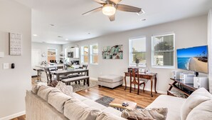 A spacious living room with a large sofa, a dining area with a table and chairs, a kitchen in the background, and a ceiling fan. - Entire House;  20 min to Beaches, Downtown Charleston, 6 min to Airport, Outlets (North Charleston)