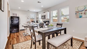 A modern kitchen with white cabinets, a built-in microwave, and a dining area with a wooden table and chairs. - Entire House;  20 min to Beaches, Downtown Charleston, 6 min to Airport, Outlets (North Charleston)