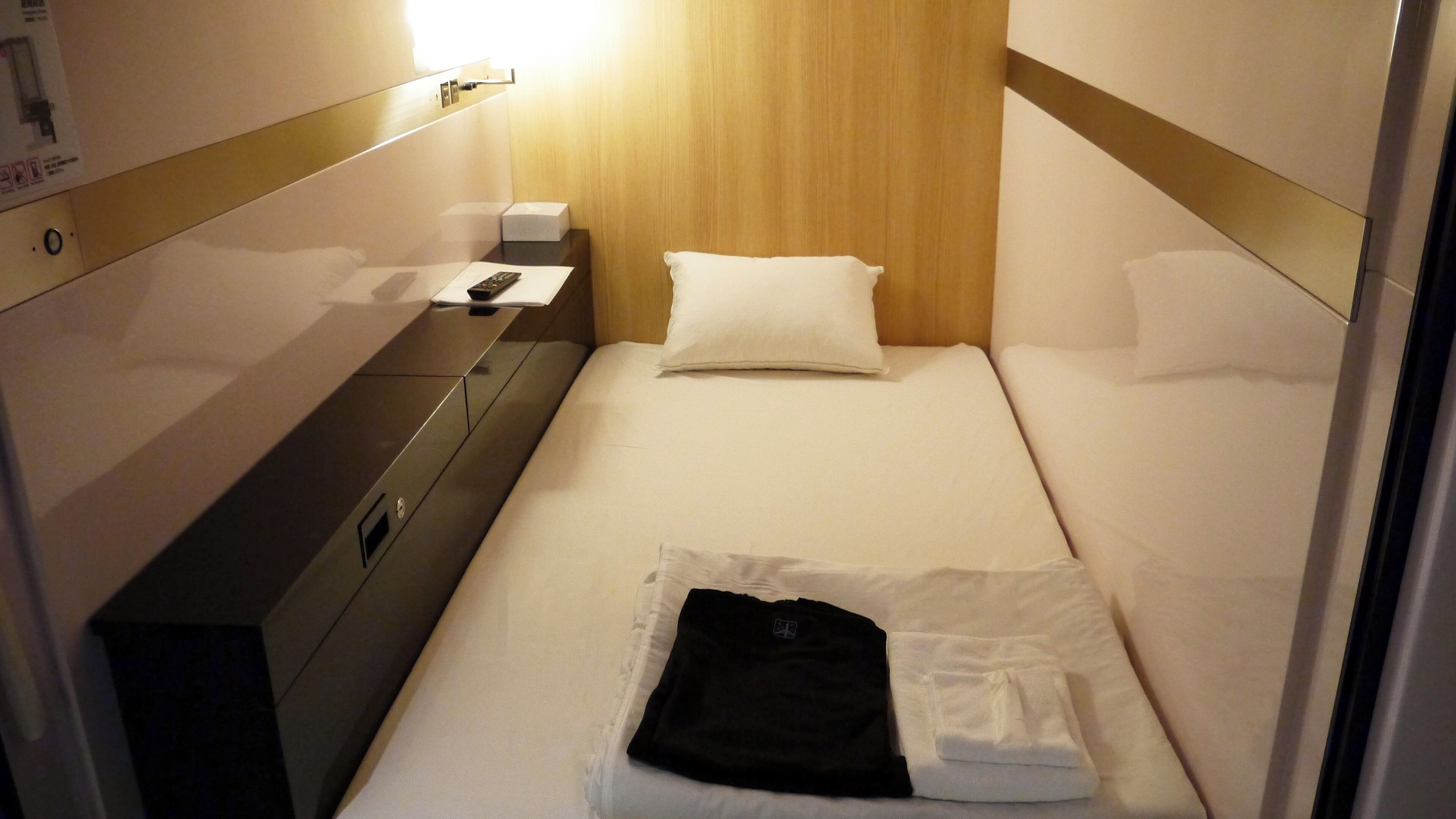 A hotel room with a bed, a bedside table, a lamp, and a wardrobe.