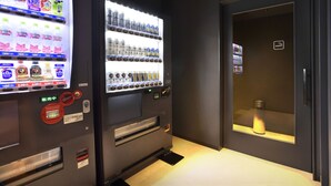 Two vending machines with various beverages and snacks, a door with a sign, and a small window with a light. - First Cabin Kansai Airport (Izumisano)