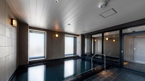 Una piscina interior moderna con paredes de vidrio transparente, suelo de baldosas e iluminación empotrada.