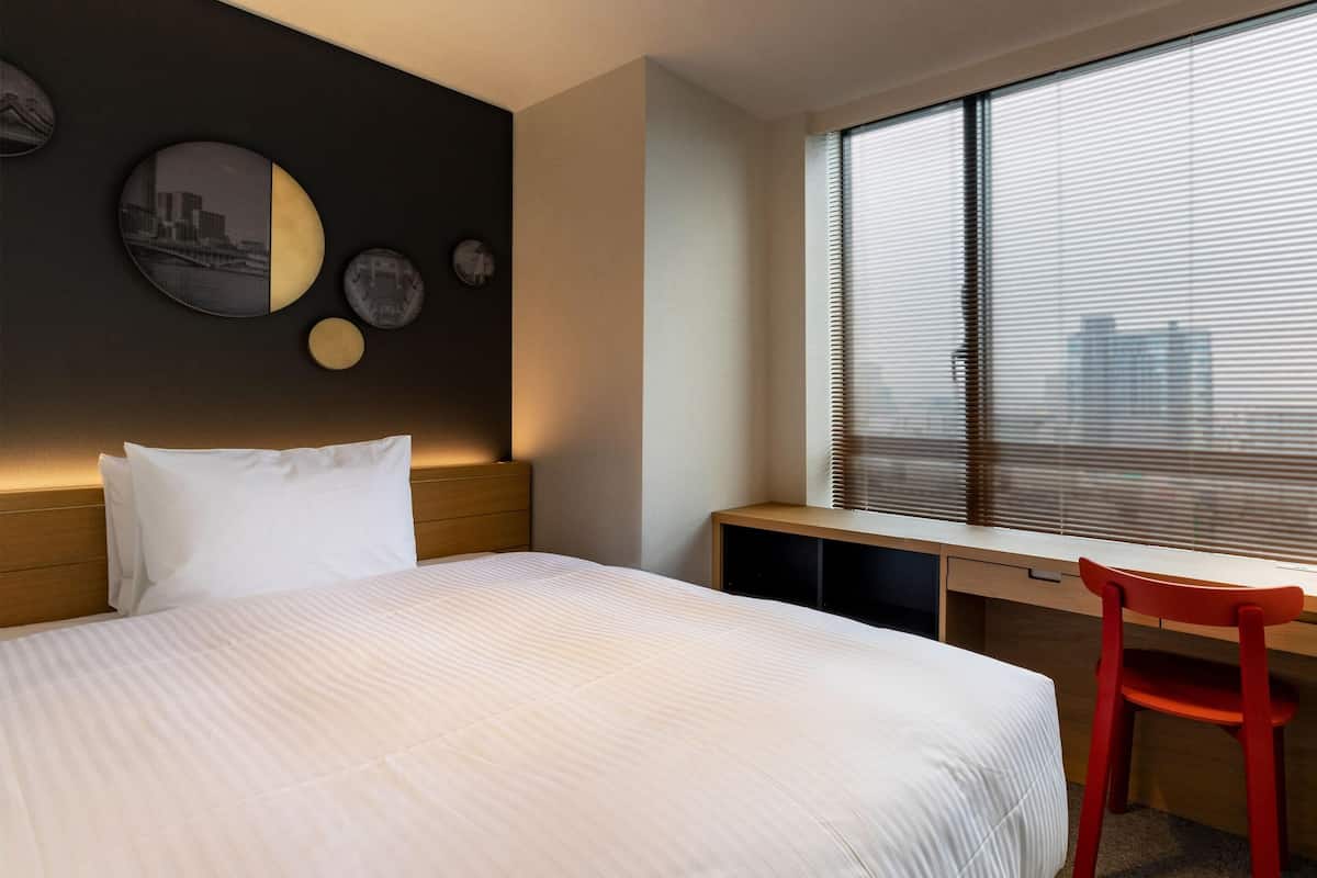 A hotel room with a bed, a desk, a chair, and a window with blinds.