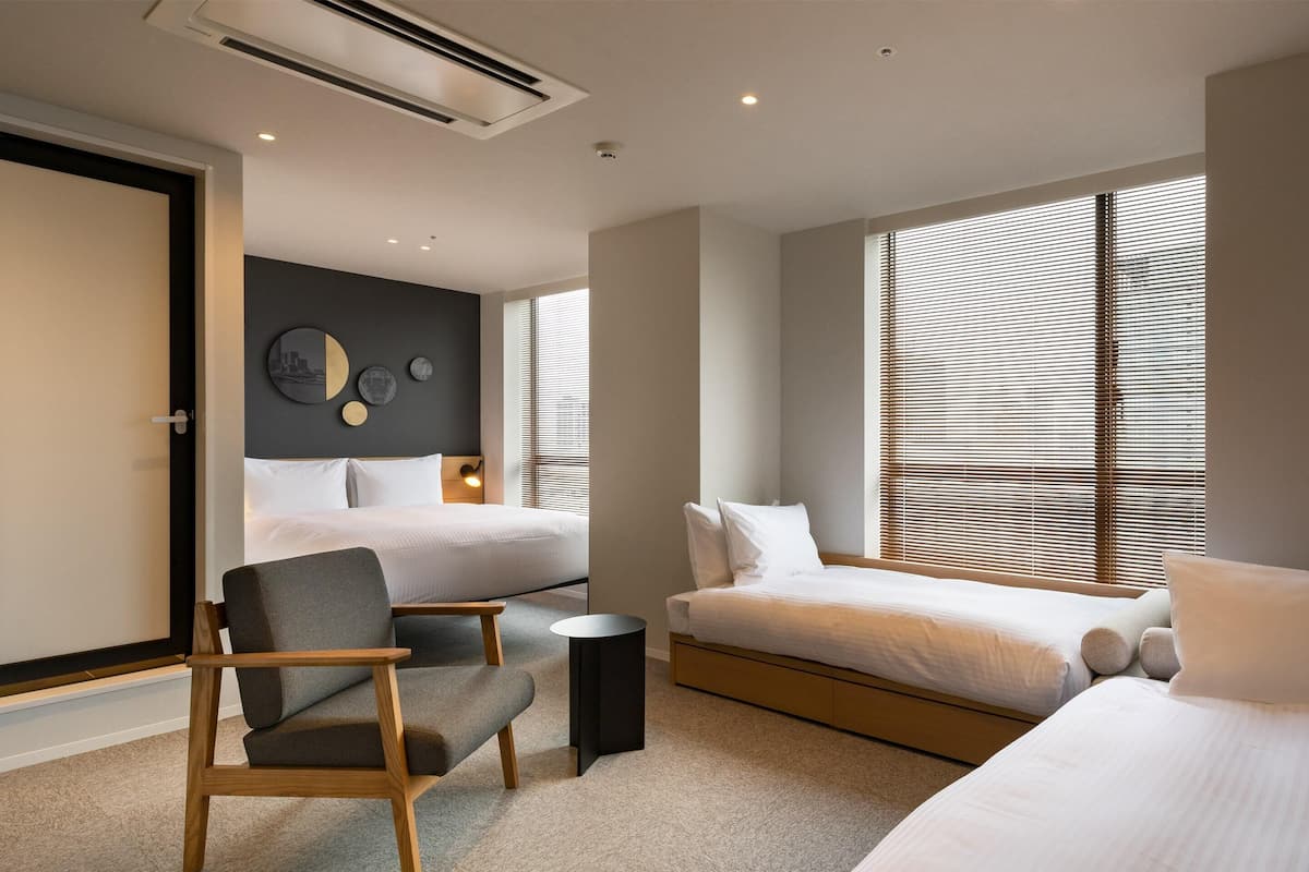 A modern hotel room with two beds, a seating area, and a large window with blinds.