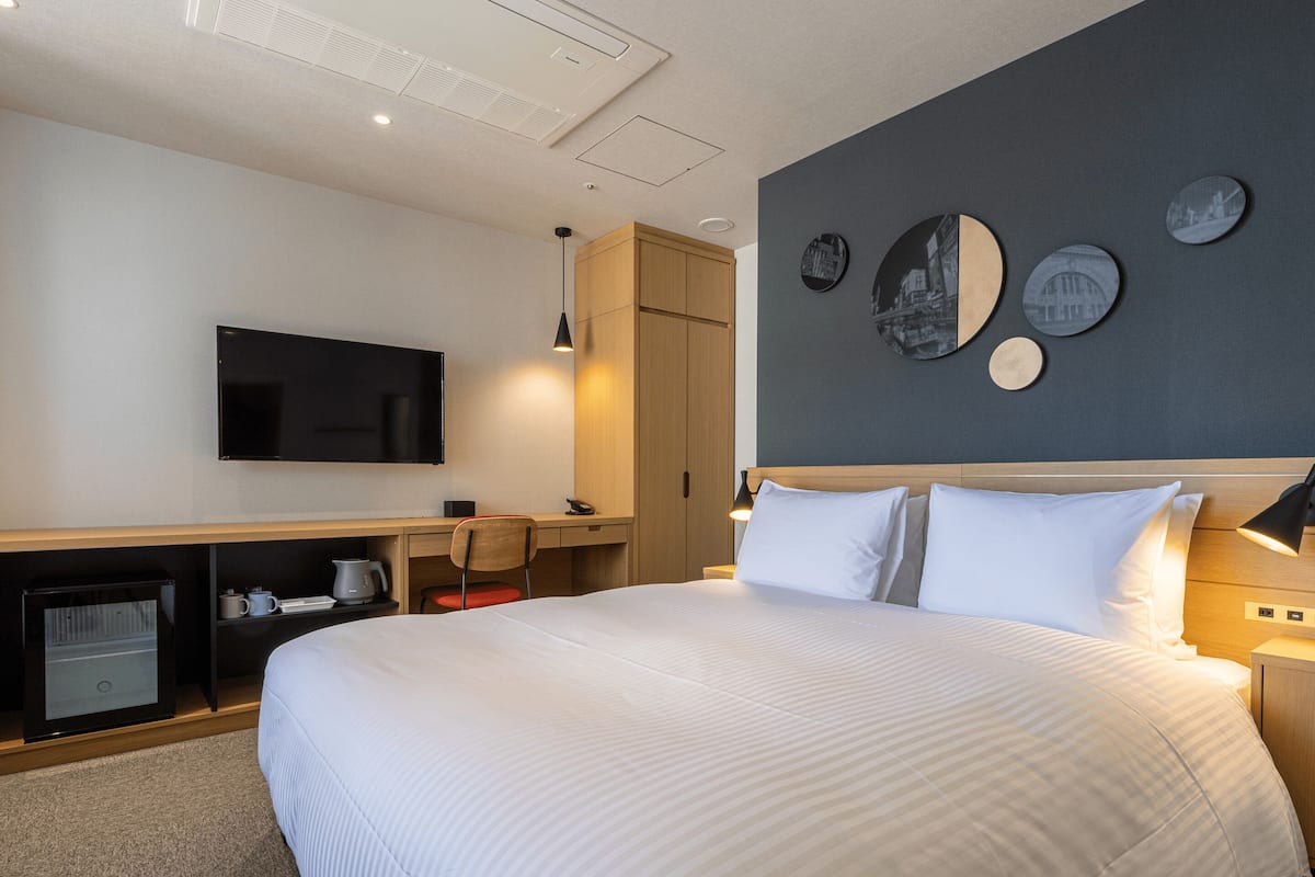 A hotel room with a large bed, a desk, a chair, a television, and a wall with decorative plates.