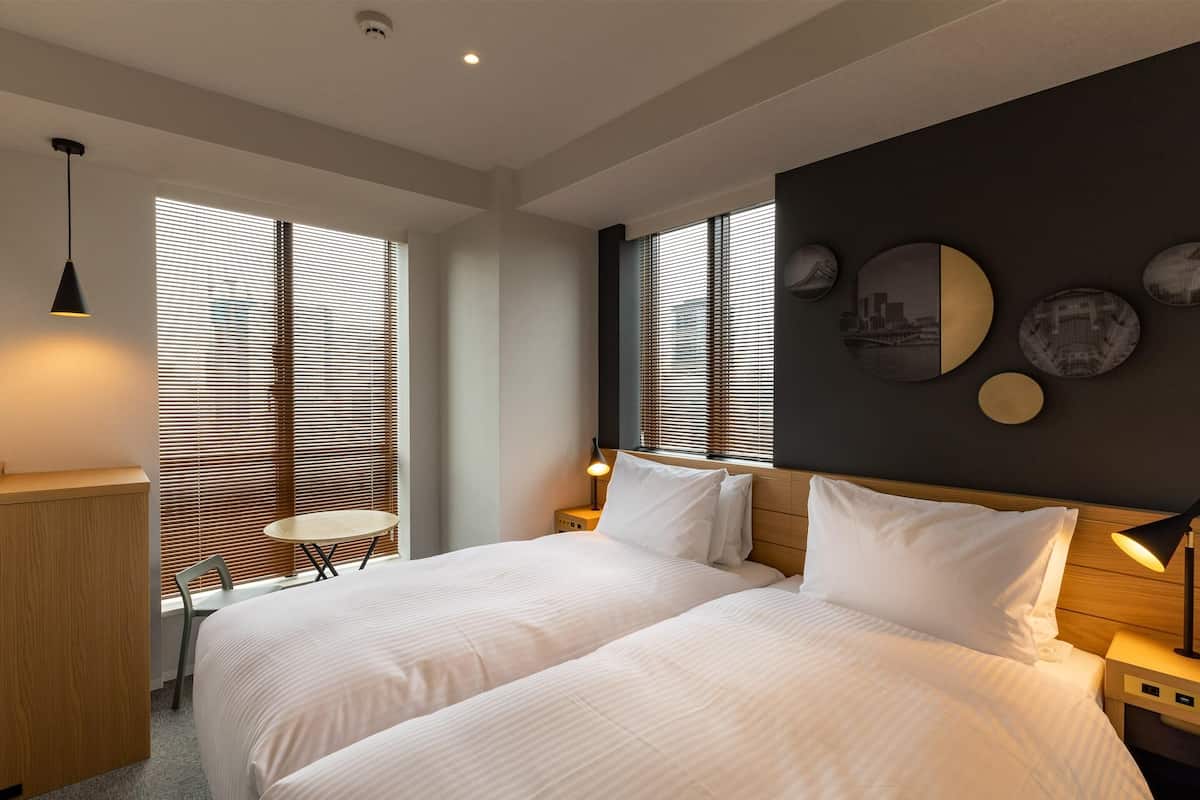 A modern hotel room with two beds, a small table, and a desk.