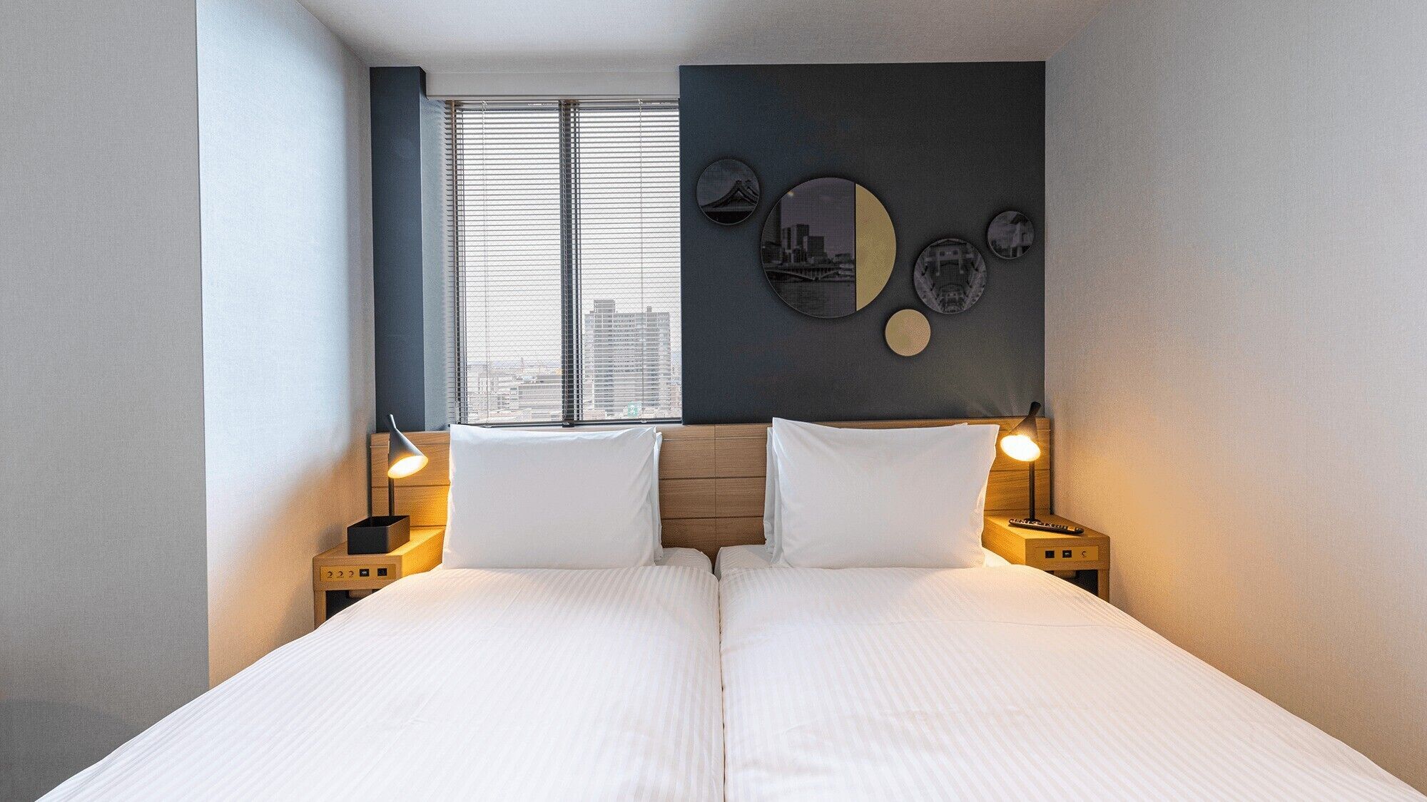 Un lit double avec deux tables de chevet, une fenêtre avec des stores et un mur orné de motifs circulaires.