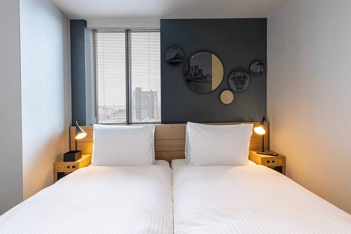 A double bed with two bedside tables, a window with blinds, and a wall with circular decor.
