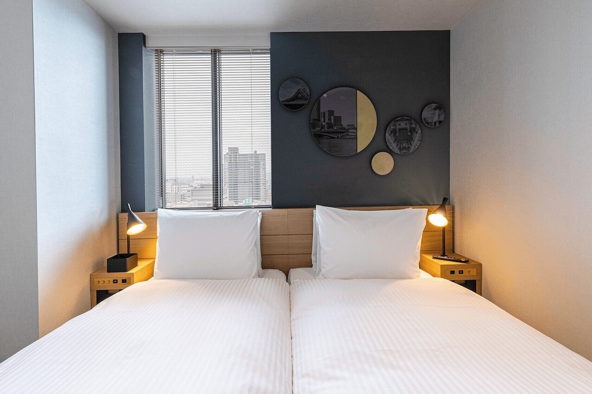 Uma cama de casal com duas mesas de cabeceira, uma janela com persianas e uma parede decorada com detalhes circulares.
