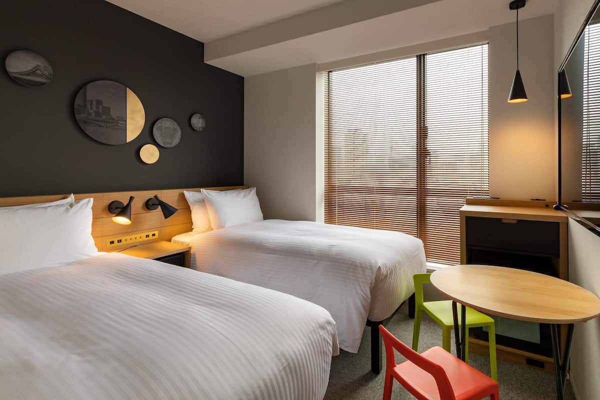 A hotel room with two beds, a small table, a chair, and a desk with a chair.