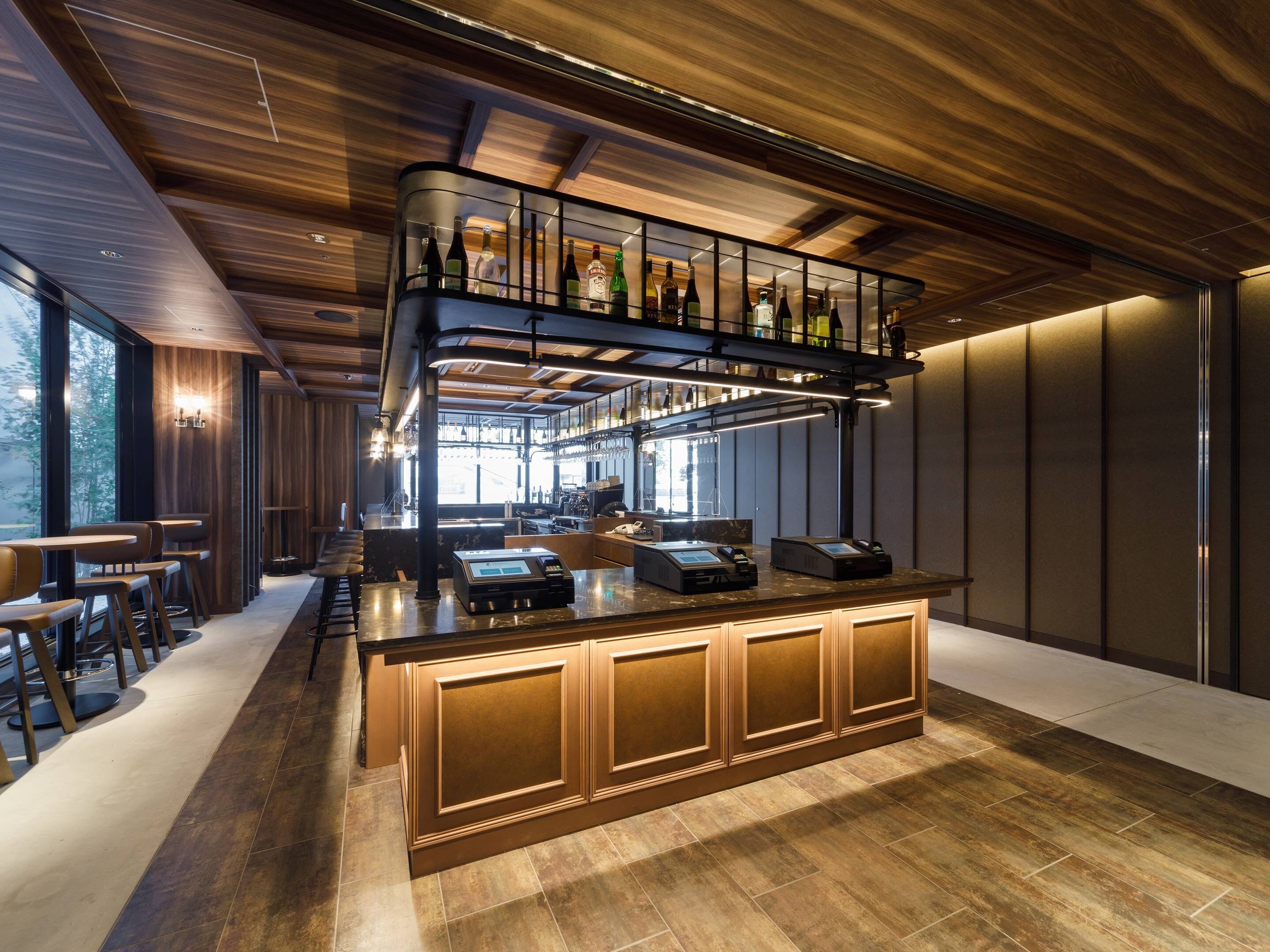 A modern bar area with a wooden ceiling, a mezzanine with bottles, and a bar counter with a cash register.