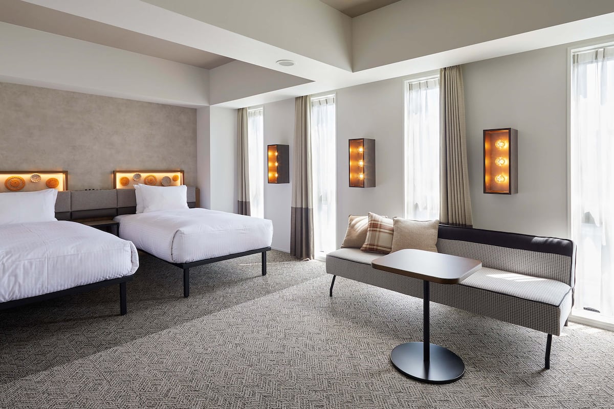 A hotel room with two beds, a sofa, a small table, and a wall-mounted light fixture.
