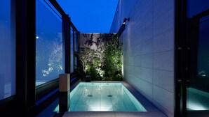 Un área de piscina interior moderna con paredes de vidrio transparente, un banco de piedra y un pequeño jardín con plantas.