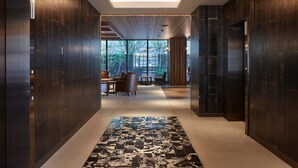 Un pasillo moderno con paneles de madera oscura, un rug con diseño y vistas a un comedor con mesas y sillas.
