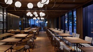Un restaurante espacioso con varias mesas y sillas, ventanas amplias e iluminación colgante moderna.