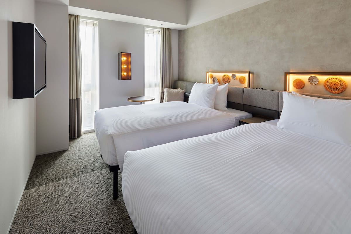 A hotel room with two beds, a TV mounted on the wall, a bedside table, and a headboard with decorative lights.