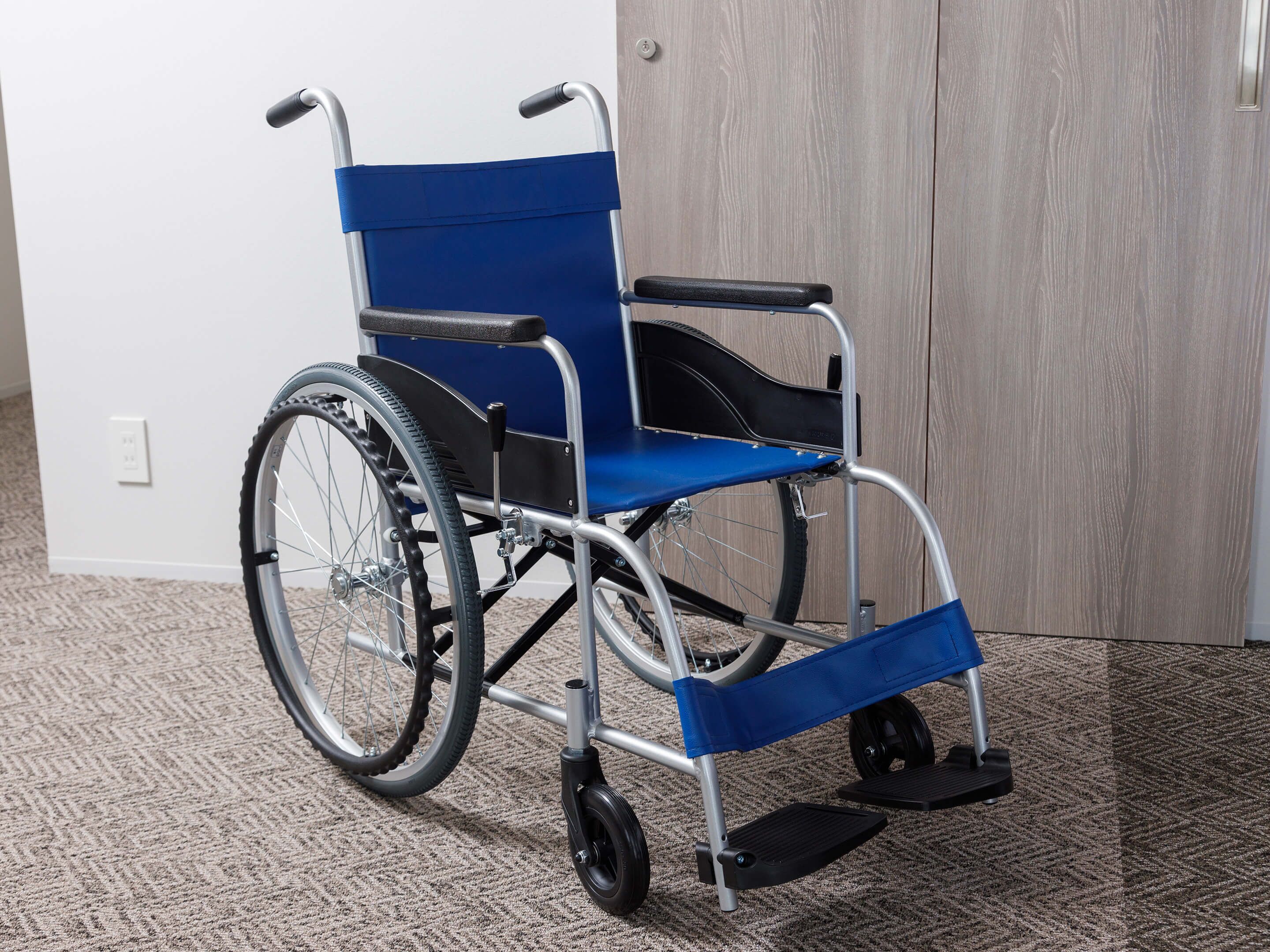 A wheelchair in a room with a carpeted floor and a wooden door in the background.