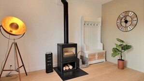 Een moderne woonkamer met een houtkachel, een driepotige vloerlamp, een klok en een potplant.
