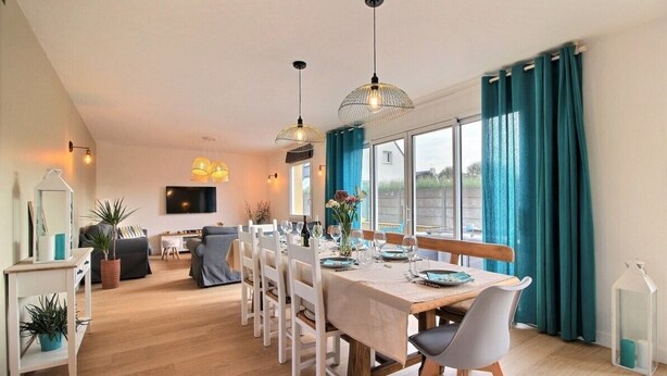 Een eetgedeelte met een lange tafel voor vier personen, witte stoelen en hanglampen.