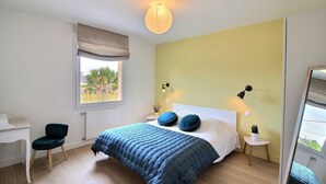 Een slaapkamer met een bed, nachtkastjes, een bureau, een stoel en een raam met uitzicht op groen.