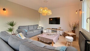 Een moderne woonkamer met een grijze bank, een bijzettafeltje, een televisie en een groot raam.