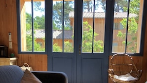 A cozy room with a wooden floor, a grey sofa, a wicker chair, and a small table with a vase.