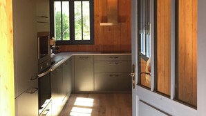 A modern kitchen with wooden walls, a built-in oven, and a window with a view of greenery.