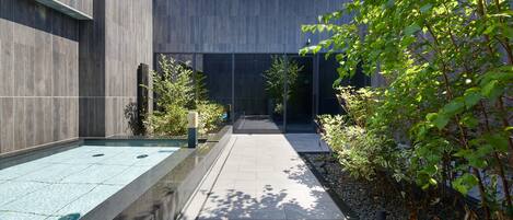 A modern outdoor pool area with a clear pathway, surrounded by greenery and a building with large windows.