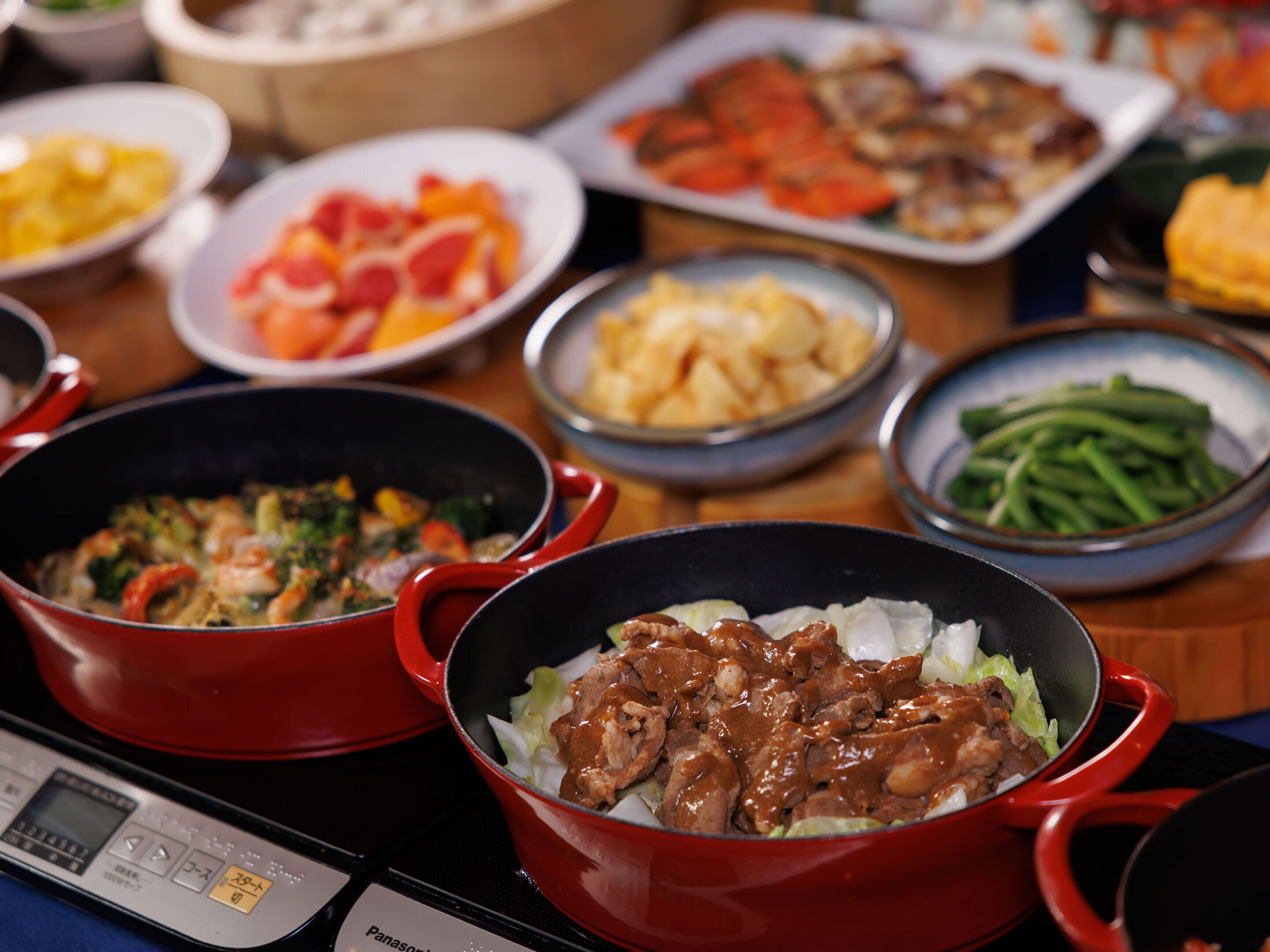 A table with various dishes, including a red pot with meat and vegetables, a bowl of green beans, and other food items.