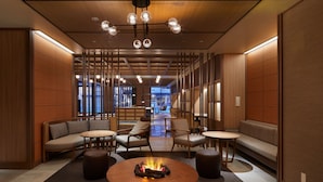 A modern lounge area with a central round table, seating arrangements, and a visible fire feature.