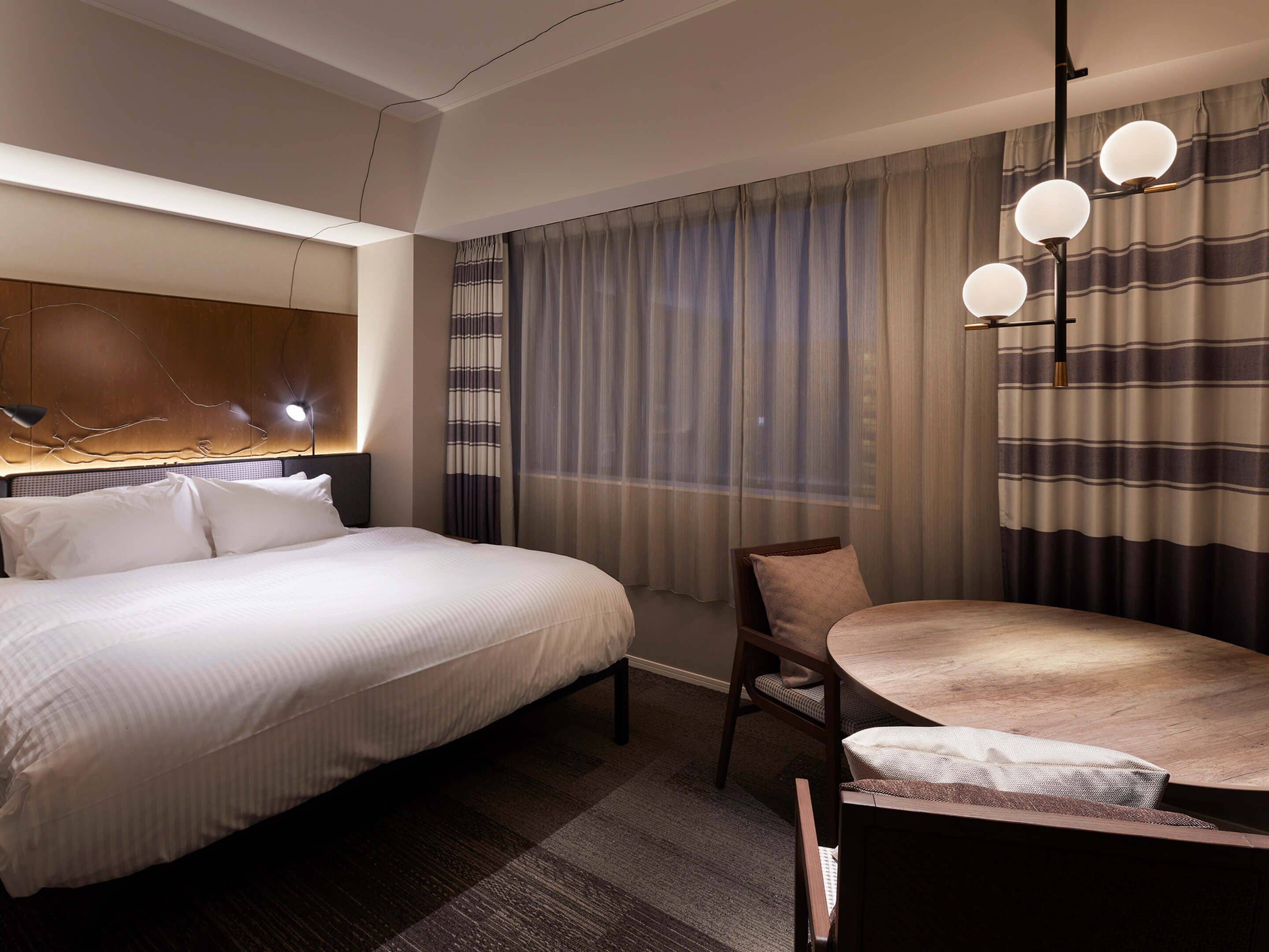 A hotel room with a large bed, a dining table, and a modern chandelier.