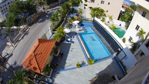 Vista aérea de um hotel com piscina, espreguiçadeiras e palmeiras.