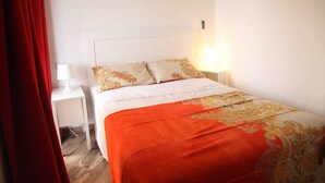 Quarto de hotel com uma cama, uma mesinha de cabeceira, um abajur e uma cortina vermelha.