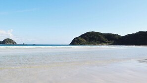 A beach with clear water, sandy shore, and a forested hill in the background. - Hotel Marinepia (Shinkamigoto)