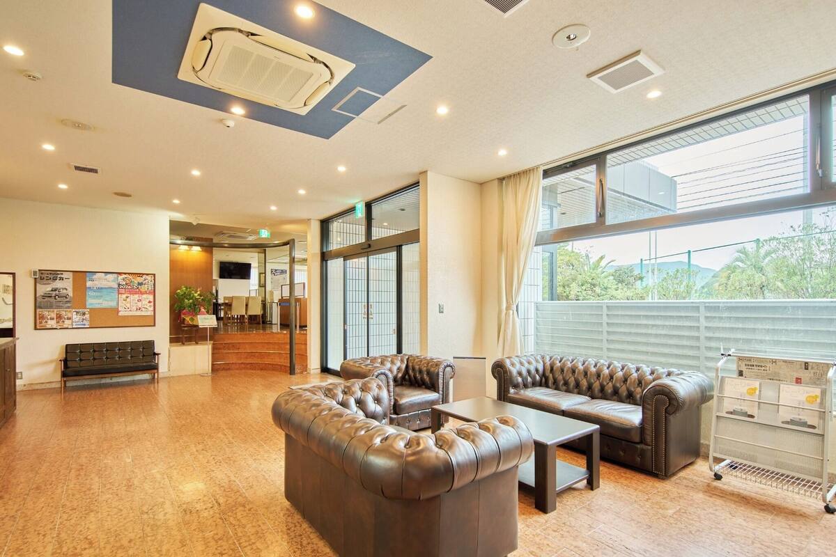 Un hall con sofás de cuero, mostrador de recepción, tablones de anuncios y ventanas amplias.