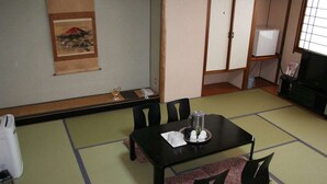 Una tradizionale stanza giapponese con pavimento in tatami, un tavolo nero con un vassoio di oggetti, sedie nere e un tavolino con cuscini.