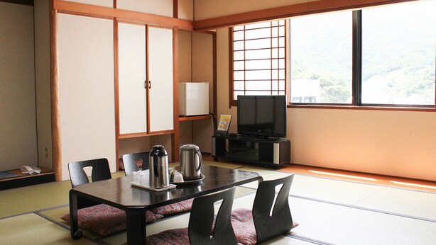 Una tradizionale stanza in stile giapponese, con pavimenti in tatami, un tavolino con cuscini, una televisione e un armadietto.