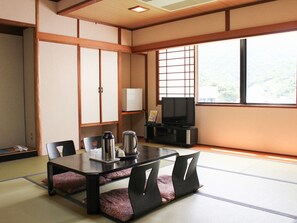 Una habitación tradicional japonesa con suelo de tatami, una mesa baja con cojines, un televisor y un armario.