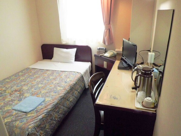Una habitación de hotel con cama, escritorio, computadora, cafetera y teléfono.