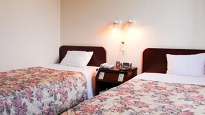 Una camera d'albergo con due letti singoli, ognuno con una coperta a fiori e cuscini bianchi. Sono presenti comodini con lampade e una sveglia digitale.