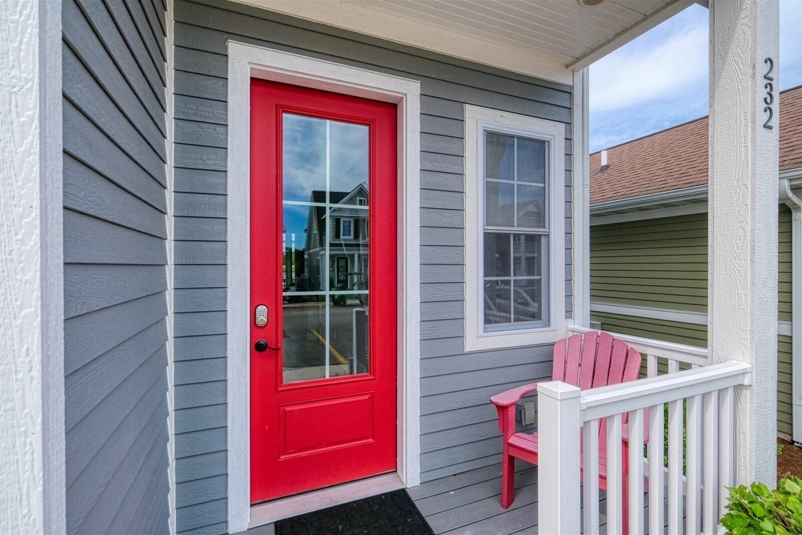 A house with a red door, a porch with a pink chair, and a mailbox.