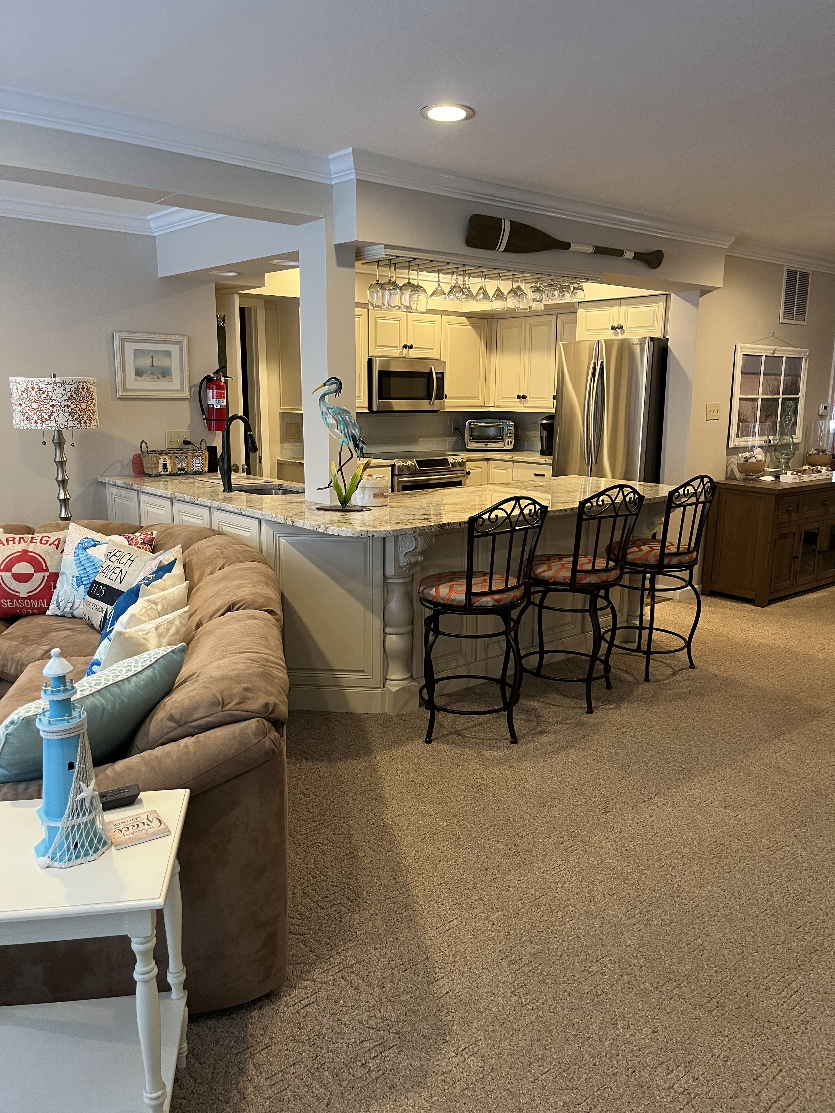 A modern kitchen with a central island, a dining area with bar stools, and a living room with a sofa and a lamp.