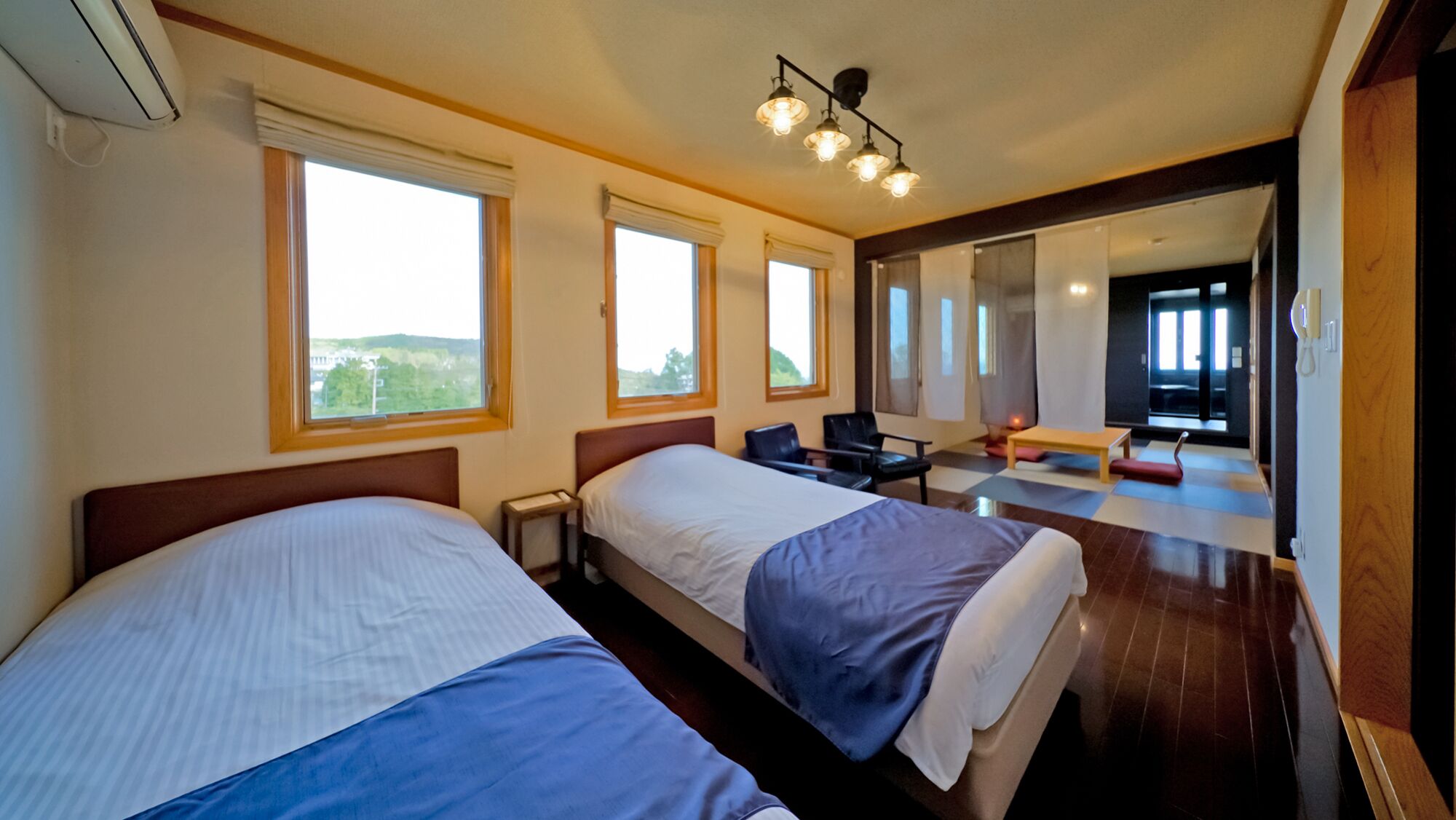 A hotel room with two beds, large windows, a desk, and a chair.