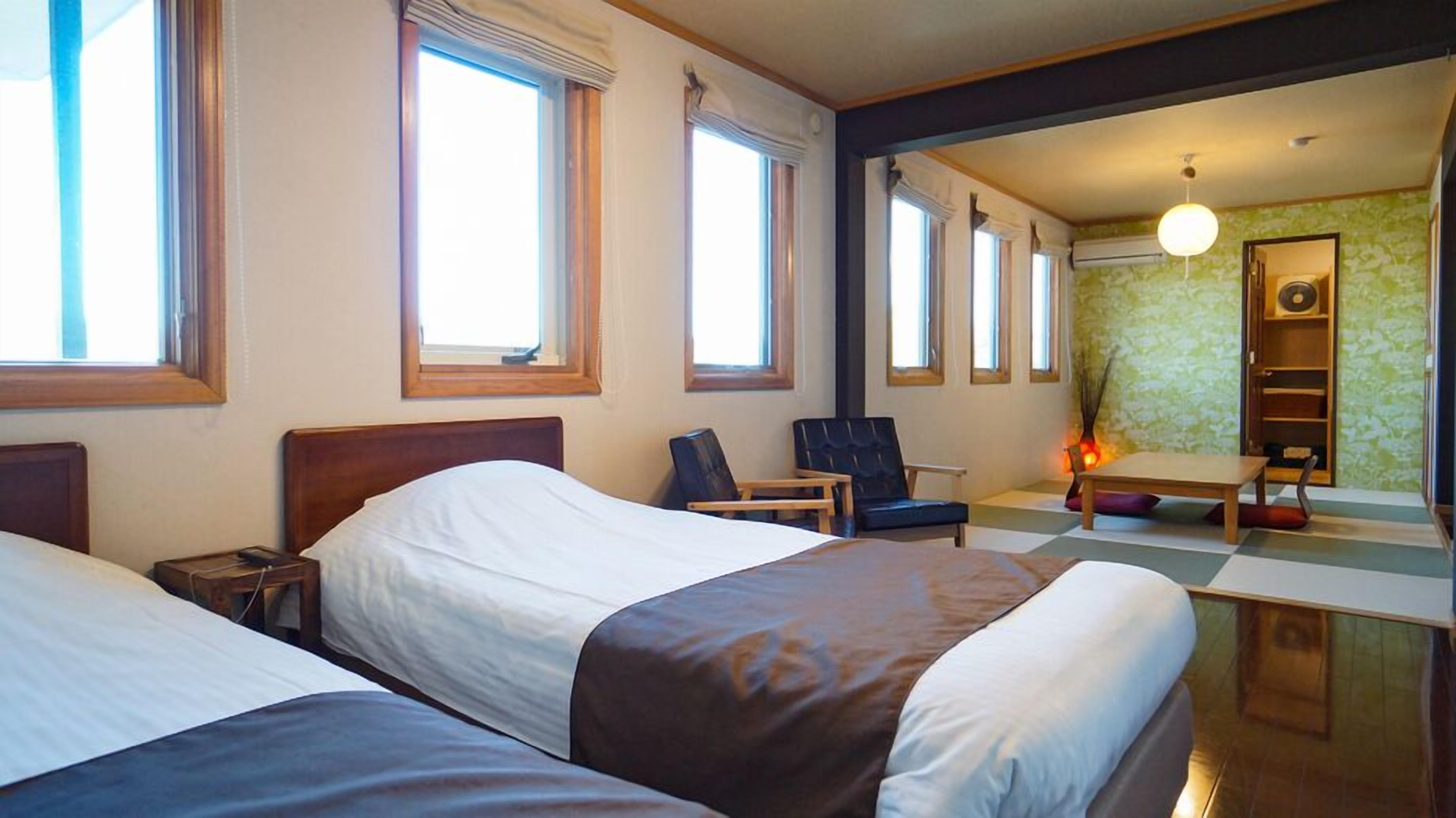 A hotel room with two beds, a desk, a chair, and a small table.