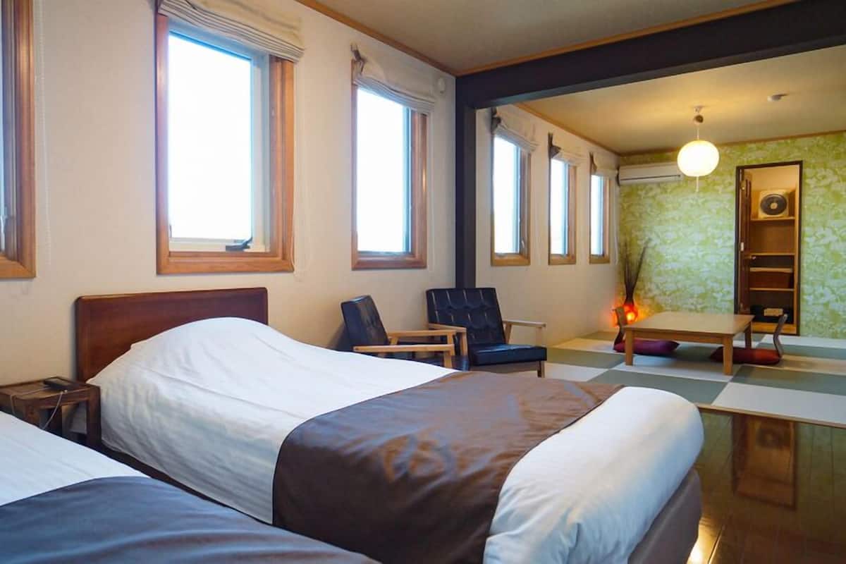 A hotel room with two beds, a desk, a chair, and a small table.